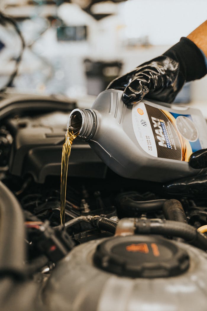 Close-up of a mechanic's gloved hand pouring engine oil into a vehicle.