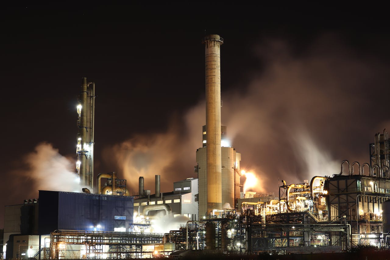 A nighttime view of an industrial factory with smokestacks emitting smoke, highlighting energy production and pollution.