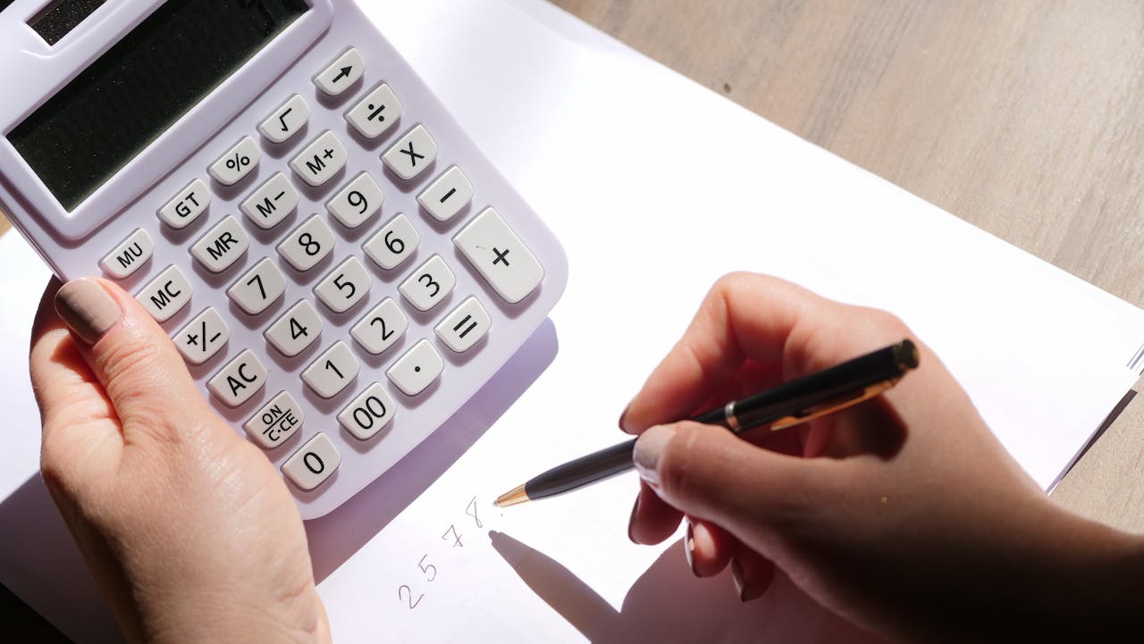 Hands using a calculator and writing numbers on paper under sunlight. Ideal for finance and education themes.